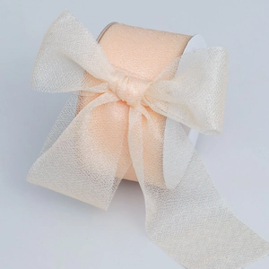 Detail view of apricot sheer organza ribbon tied in a bow on a white paper spool