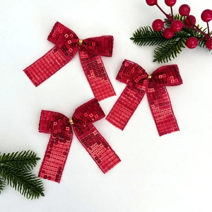 Dettaglio di fiocchi di Natale in paillettes rosse con nastri dorati e decoro di bacche