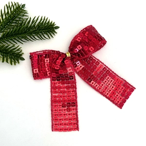 Dettaglio di un fiocco di Natale festivo con paillettes rosse e chiusura dorata su pino