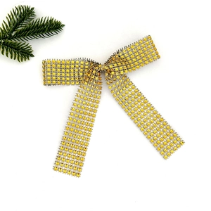 Golden rhinestone bow with silver mesh base and festive pine branch on white background