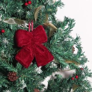 Close-up of a burgundy velvet Christmas bow hanging on a festive tree with pine cones