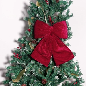 Close-up of a large burgundy velvet bow hanging on a Christmas tree with festive decor