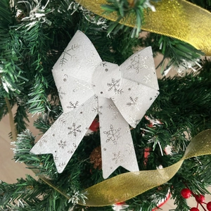 Close-up of white Christmas bow with silver snowflakes hanging on a festive pine tree