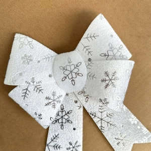 Close-up of white fabric Christmas bow featuring elegant silver snowflake patterns