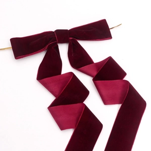 Close-up of a burgundy velvet bow with long ribbons and a gold metal clip for festive decor