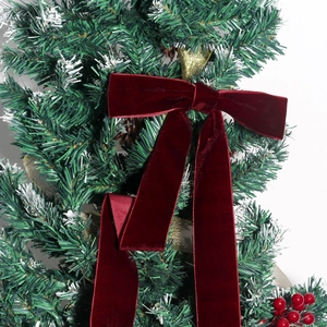 Large burgundy velvet Christmas bow on decorated tree with pine cones and golden ribbons