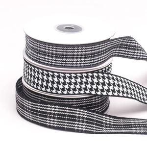 Close-up of black and white houndstooth and checkered ribbons stacked on white spools