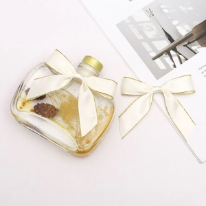 Elegantly crafted 2cm gold-edged cream bow on glass aromatherapy bottle with dried flowers