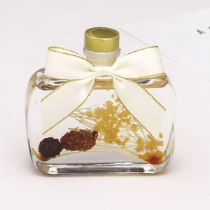 Flat glass bottle with yellow dried flowers and a gold-edged cream satin ribbon bow