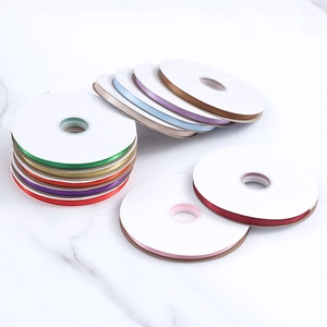 Multiple rolls of 1cm colorful polyester satin ribbons on a white marble surface