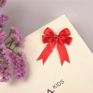 Macro shot of red satin ribbon bow with golden edge detail on a neutral display surface