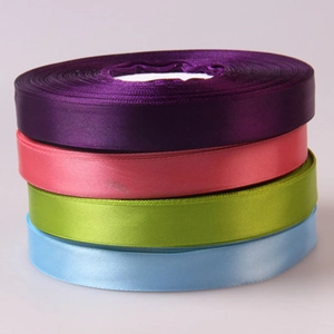 Close-up of four satin ribbon rolls in purple, pink, green and blue with glossy texture