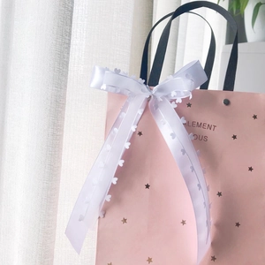 Pink gift bag with star pattern featuring a white satin bow and heart-shaped lace detail