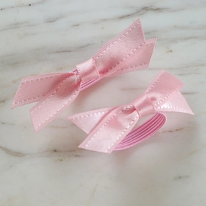 Pair of pink satin bow hair ties with embossed edges on a high elastic rubber band