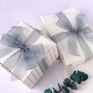 Close-up of elegant white gift box with 2.5cm grey organza ribbon and green leaf accents