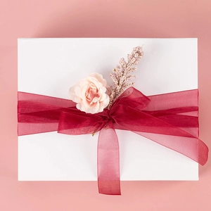 Close-up of a white gift box decorated with burgundy organza ribbon and pink fabric flowers