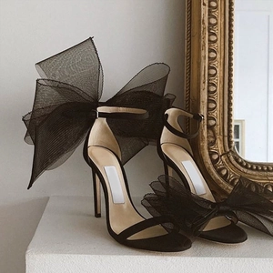 Detail of elegant black satin high heels featuring oversized mesh bows and ankle straps
