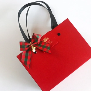 Red Christmas gift bag with festive bow, gold bell, and LOVE tag on white background