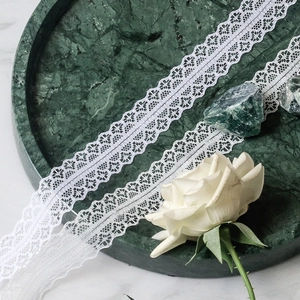 Detailed view of 3cm white floral lace trim on a dark marble tray with a white rose