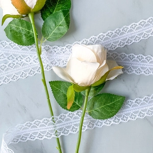 Detail of 3cm wide white lace ribbon beside artificial cream silk rose bouquet