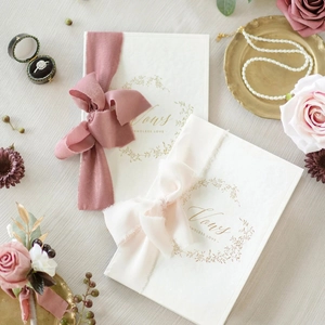 Detailed view of white wedding vow books with gold wreath and frayed chiffon ribbons