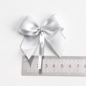 Silver satin ribbon bow with glitter edges and wire tie shown with ruler for scale