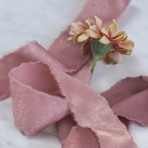 Close-up of vintage dusty rose velvet ribbon with frayed edges on marble surface