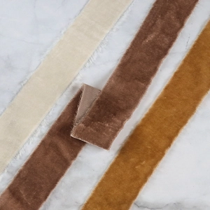 Macro detail of frayed velvet ribbons in cream, tan, and gold on marble background