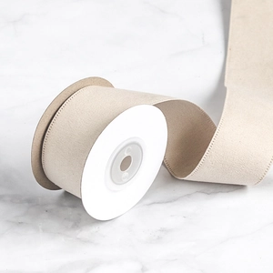 Close-up of beige velvet ribbon roll with textured edges on marble background