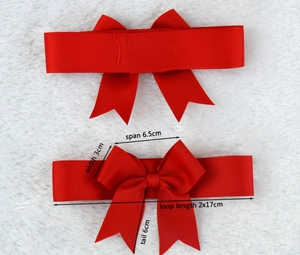 Detail of red grosgrain ribbon bow with specific dimensions on a white plush background