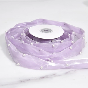 Macro detail of purple organza ribbon with white pearls and silver studs on white marble