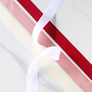 Detalle de cintas de poliéster con textura de rombos en crema, rosa, rojo y blanco sobre mármol