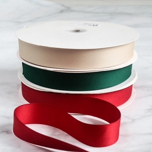 Rouleaux de ruban de satin mat champagne, vert foncé et rouge sur fond de marbre