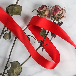 Close-up of vibrant red satin ribbon elegantly draped over withered roses on marble