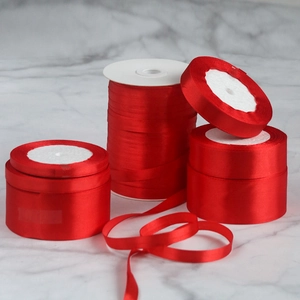Detail of glossy red satin ribbons in various widths on white rolls with smooth texture