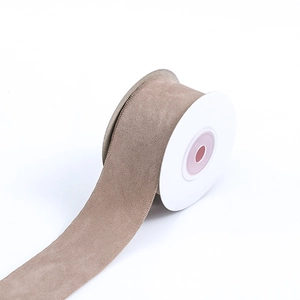 Macro shot of faux suede ribbon in taupe color with stitched edges on a white spool