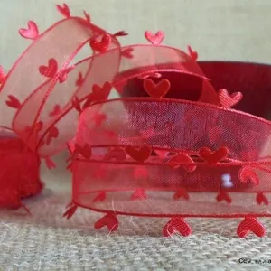 Détail macro d'un ruban organza rouge avec bords cœurs sur fond en toile de jute