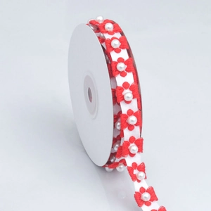 Close-up of embroidered plum blossom ribbon with white pearls on a white plastic spool
