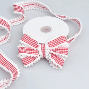 Macro detail of red gingham ribbon with white pom-pom trim for DIY hair bow accessories
