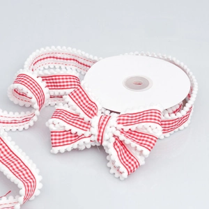 Detail of red and white gingham ribbon with white pom pom edges tied in a bow on spool