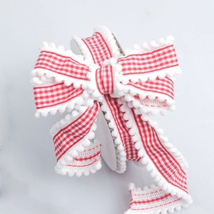 Detailed view of red and white plaid ribbon with soft white pom-pom fringe trim