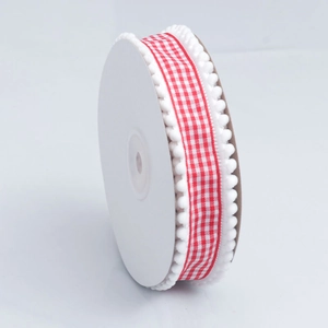 Detail of red and white plaid ribbon with white pom-pom trim on a white spool