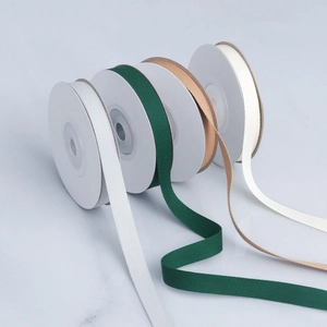 Close-up of herringbone cotton ribbons in white, green, camel, and beige rolls