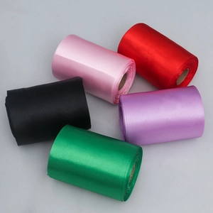 Close-up of five colored satin ribbons on rolls showing smooth glossy silk texture