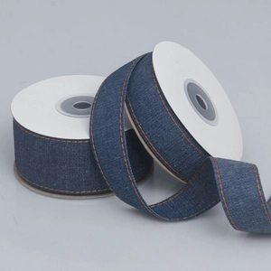 Close-up of dark blue denim ribbon with orange double stitching on white spools
