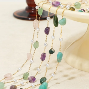 Golden chain necklace with colorful irregular gemstones and white pearls hanging on stand