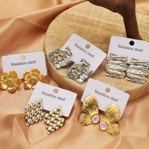 Elegant stainless steel earrings set featuring floral and bow designs on a wood base