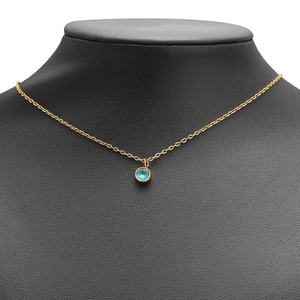 Minimalist gold necklace with a round blue crystal pendant on a black model stand
