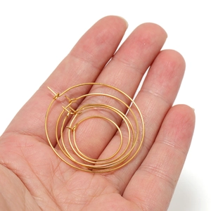Four pairs of polished gold hoop earrings in varying sizes displayed on a palm