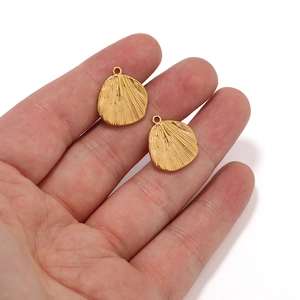 Golden stainless steel fan-shaped pendants with radial texture held on fingertips